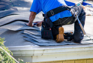 Roofing contractor kneeling on the roof of a home as he replaces asphalt shingles